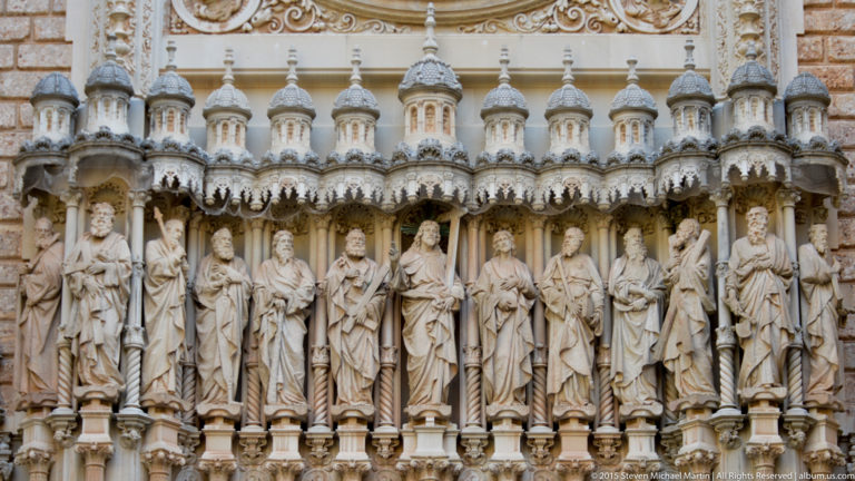 Row of Christ and Apostle statues beneath ornate carved canopies on the façade of Montserrat basilica.