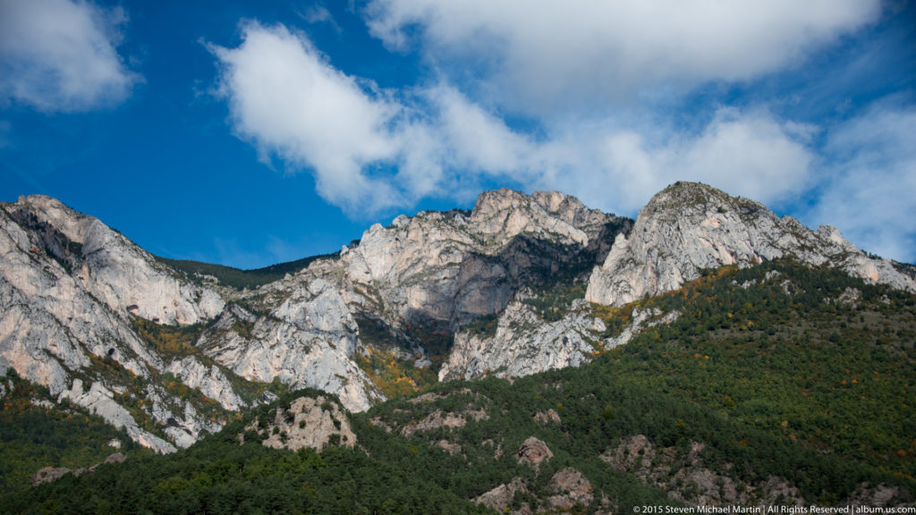 Broad pale Montserrat ridgeline rises above dark green forest beneath blue sky and white clouds.