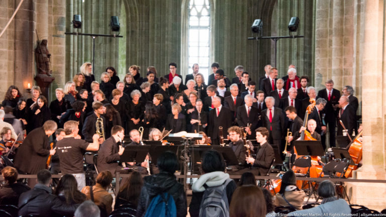 Choir and orchestra performing before an audience inside Mont Saint-Michel’s stone abbey church.