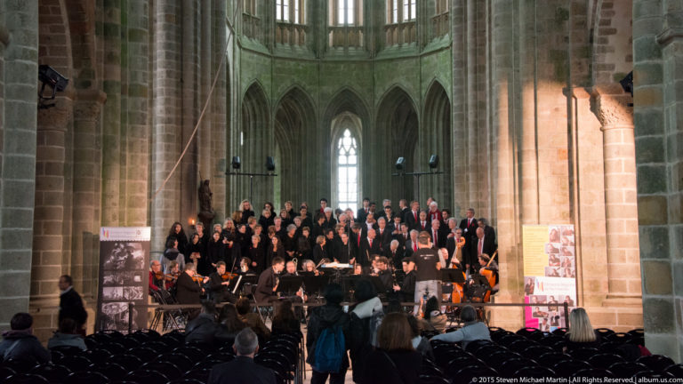 Distant choir and orchestra performing inside the abbey church, with empty seating and visitors in the foreground.
