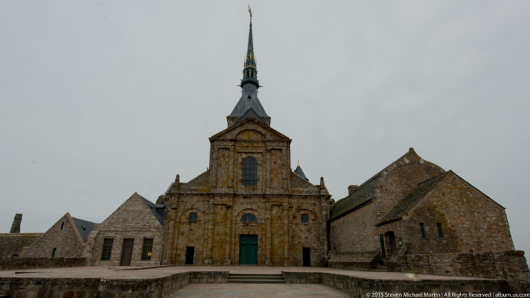 Oblique view of the abbey church façade with adjoining stone buildings and roofs.