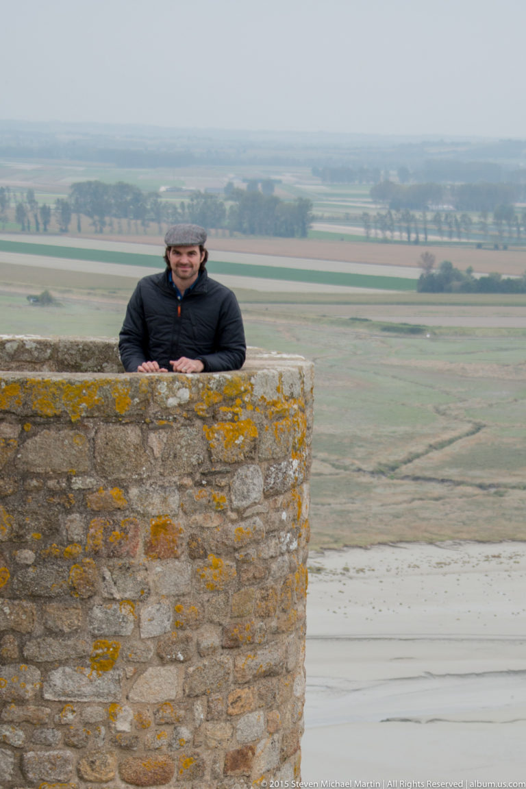 Visitor standing behind the parapet of a square stone tower with fields in the distance.