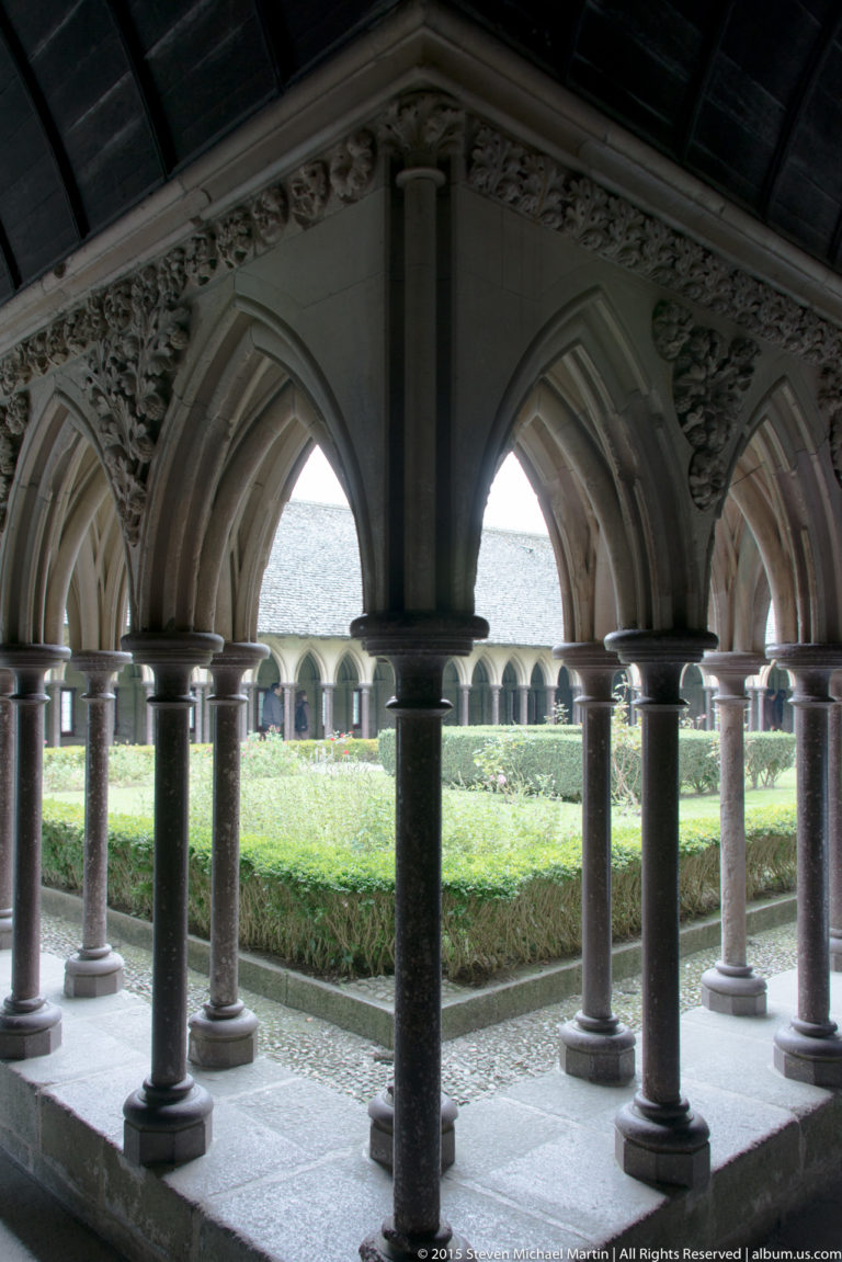 Pointed cloister arches and slender columns framing the green central garden at Mont Saint-Michel.