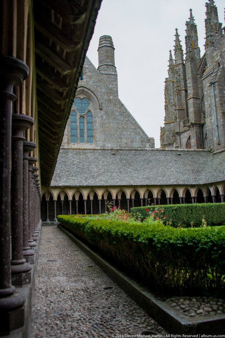 Cloister garden and arcade with stone abbey buildings and the church rising beyond.