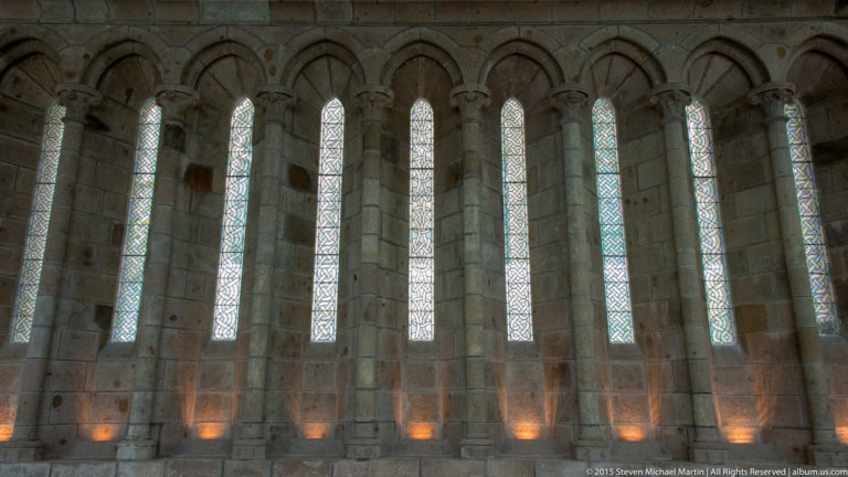 Row of tall narrow windows set in a thick stone wall inside Mont Saint-Michel Abbey.