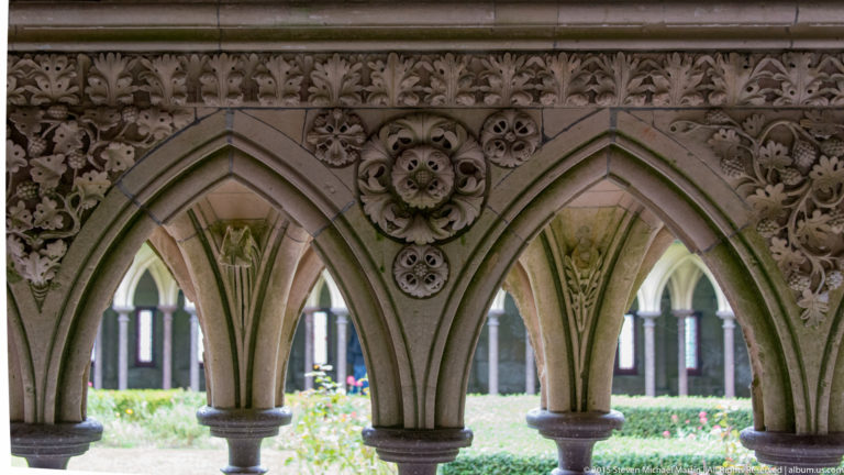 Close view of carved pointed cloister arches and slender columns with garden visible beyond.