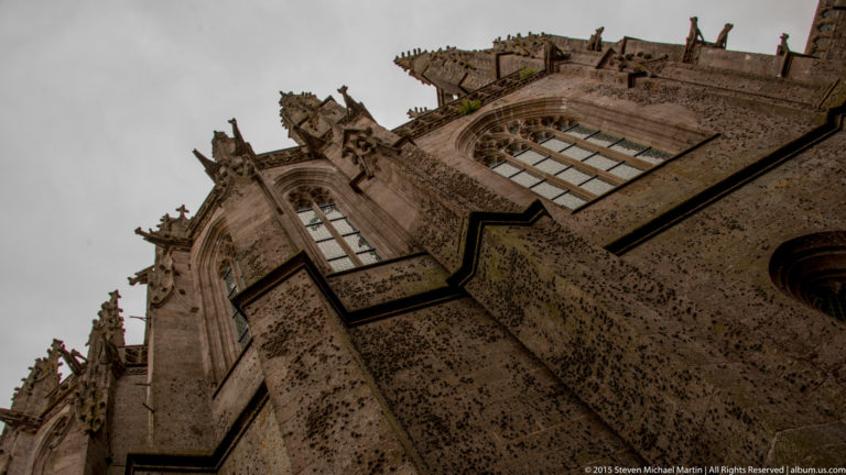 Steep upward view of tall abbey church walls and windows against an overcast sky.