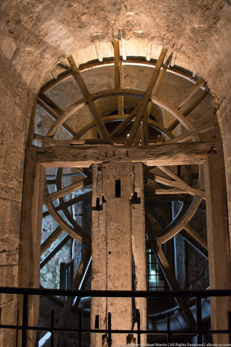 Rear view of a large wooden treadwheel and timber lifting mechanism mounted within stone walls.