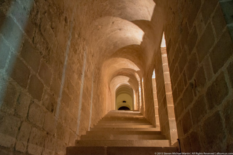 Long narrow vaulted stone corridor receding through repeated arches inside Mont Saint-Michel Abbey.