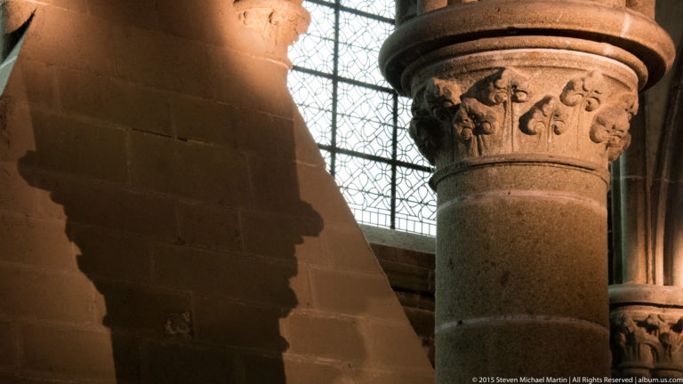 Carved stone capital with shallow foliate ornament on a cylindrical column beside a window.