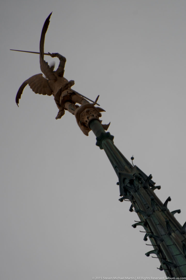 Low-angle view of the gilded winged Saint Michael statue at the top of the abbey spire.