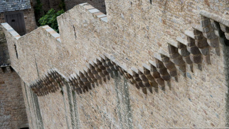 Rows of projecting stone corbels beneath the upper edge of a fortified masonry wall.