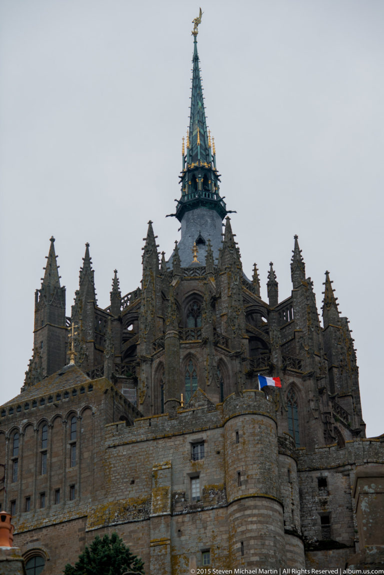 Low-angle exterior view of Mont Saint-Michel Abbey with pinnacles, stone terraces, and the spire above.