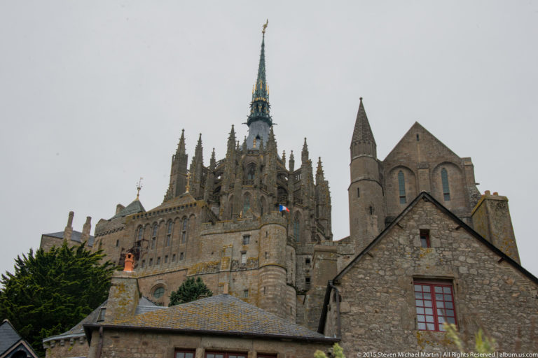 Mont Saint-Michel Abbey and spire rising above lower stone village buildings.
