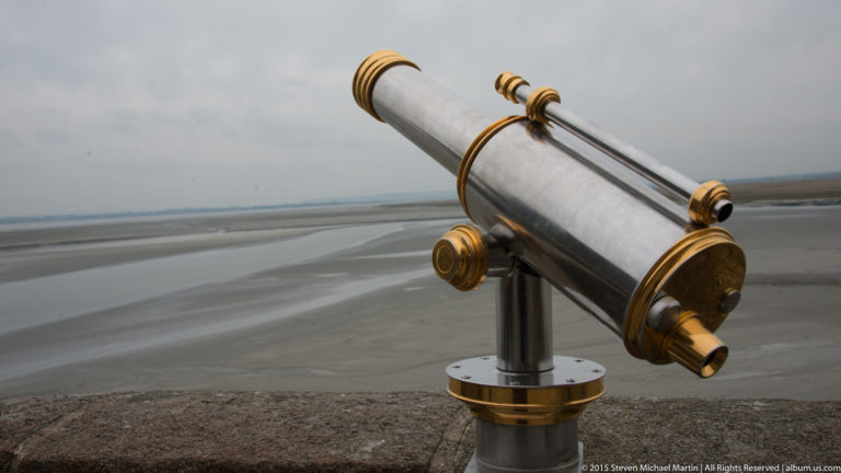 Long metal viewing telescope with brass fittings aimed across the tidal flats.