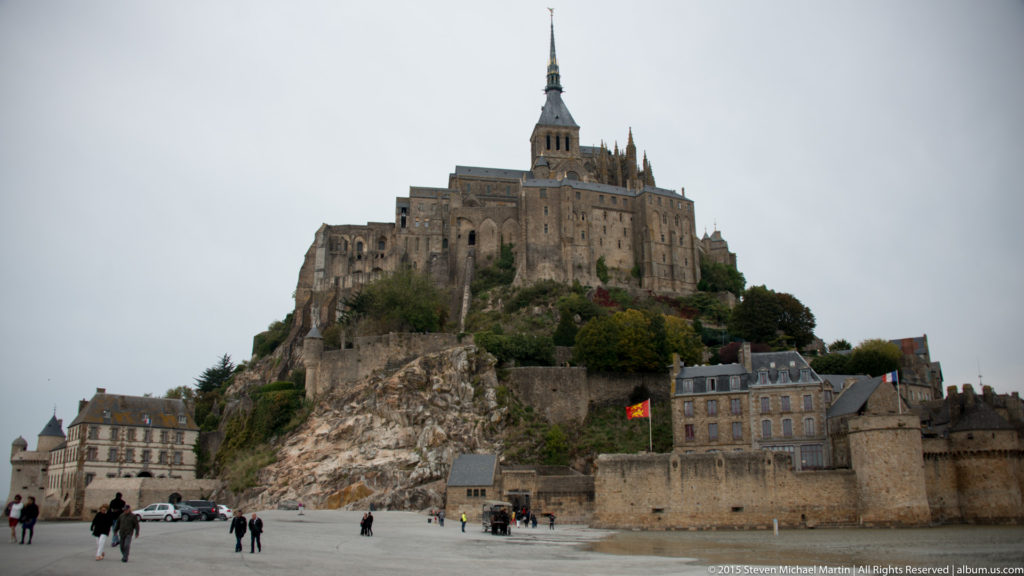 Mont Saint-Michel rising from the tidal flats with people on the approach and the abbey above.