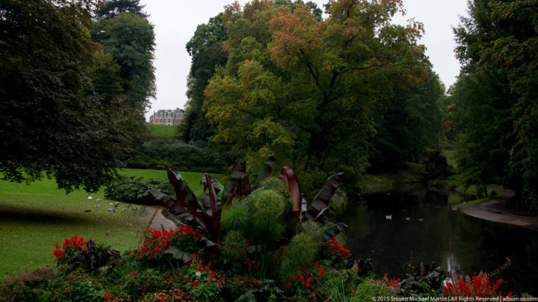 Ornamental pond bordered by lawns, mature trees, red flowers, and large-leaved plants in a landscaped Nantes park.