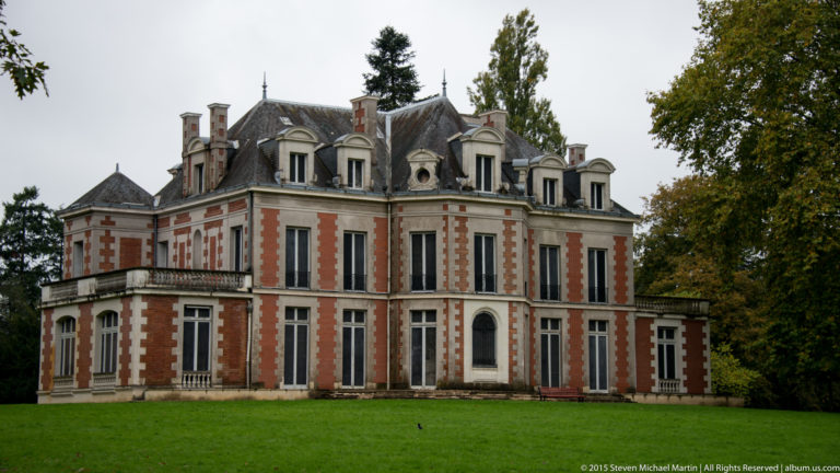 Close oblique view of a red-brick château with pale stone quoins, tall windows, dormers, chimneys, and a steep slate roof.