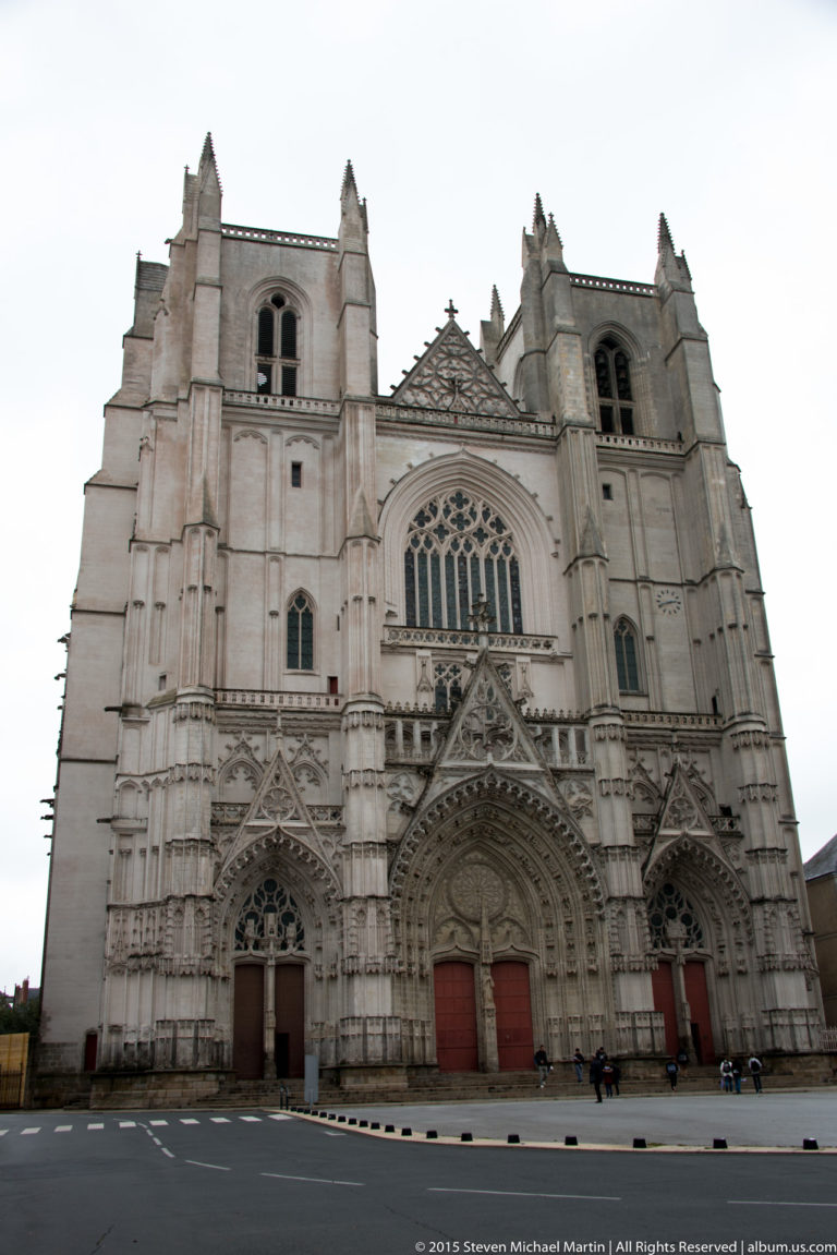 West façade of Nantes Cathedral with twin square towers, three portals, buttresses, and a large central Gothic window.