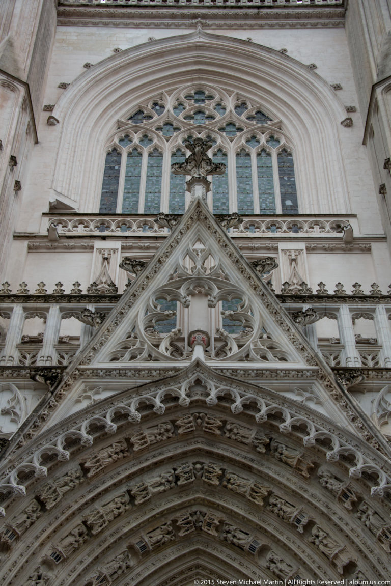 Upward view of a Nantes Cathedral portal with pointed gable, Gothic tracery, carved archivolts, and layered stone ornament.