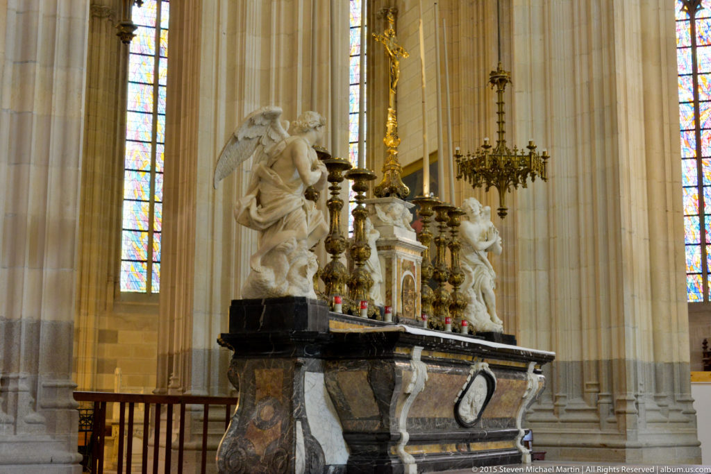 Dark marble side altar in Nantes Cathedral with white sculpted angels, gilded candlesticks, and stained glass behind.