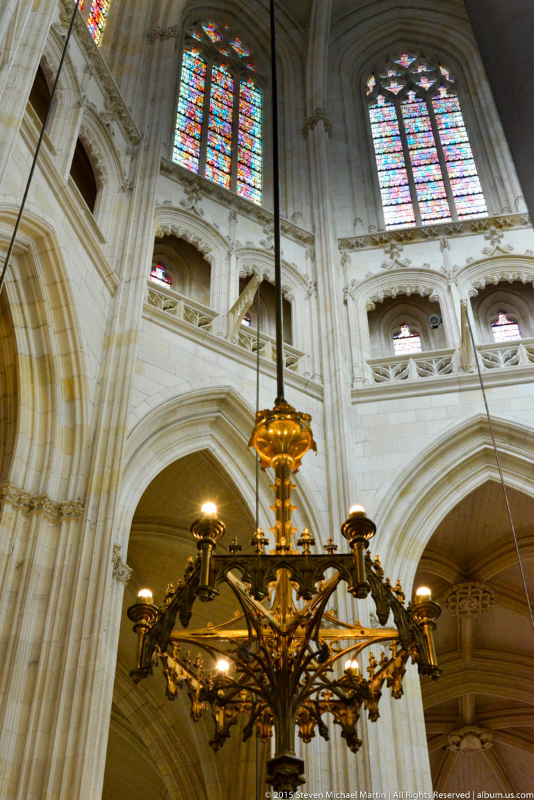 Large branching metal chandelier hangs beneath upper arcades and stained-glass windows inside Nantes Cathedral.