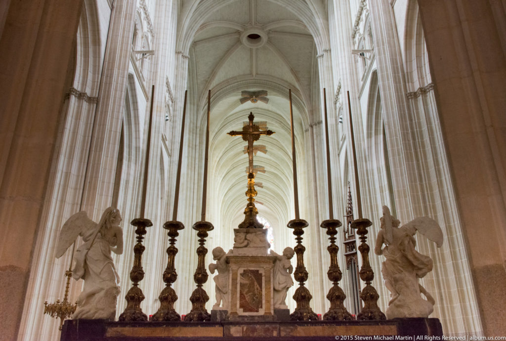 Ornate altar in Nantes Cathedral with two white angels, tall candlesticks, a gilded cross, and high ribbed vaults behind.