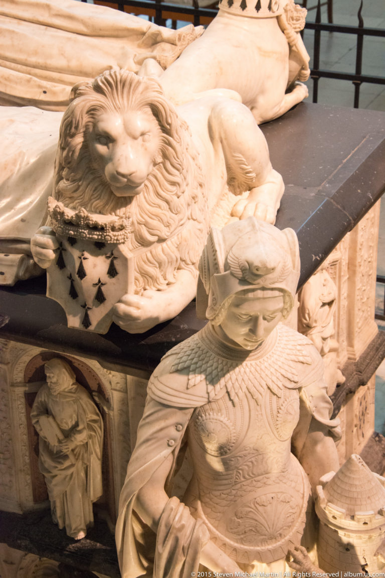 Carved lion with an ermine-patterned heraldic shield beside a kneeling female figure on the ducal tomb in Nantes Cathedral.