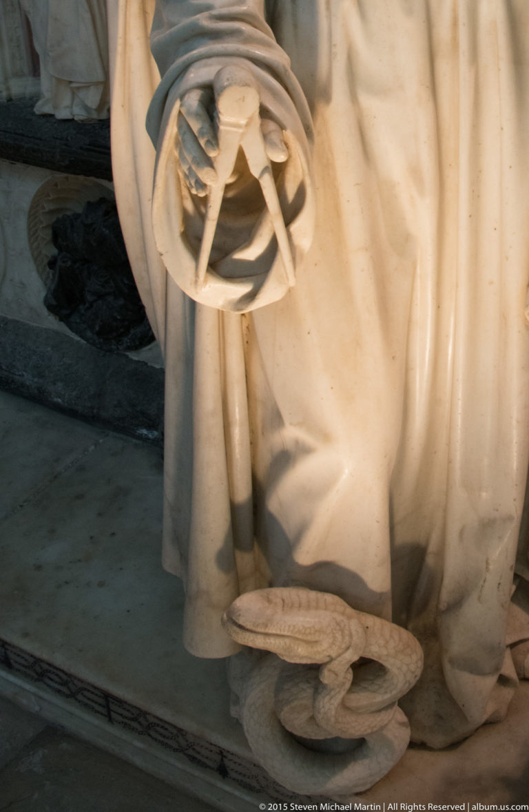 Close detail of a carved compass or dividers held against the drapery of an allegorical figure on the ducal tomb.