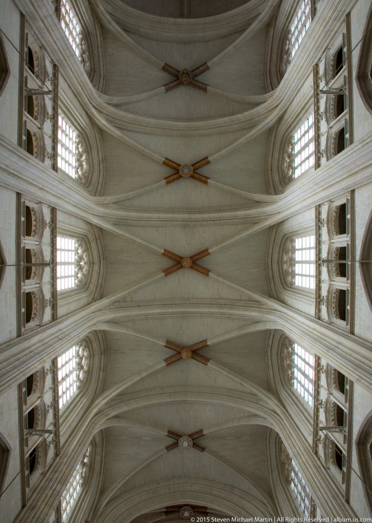 Upward view of Nantes Cathedral's repeating pale ribbed vaults with clerestory windows and decorative intersections along the nave ceiling.