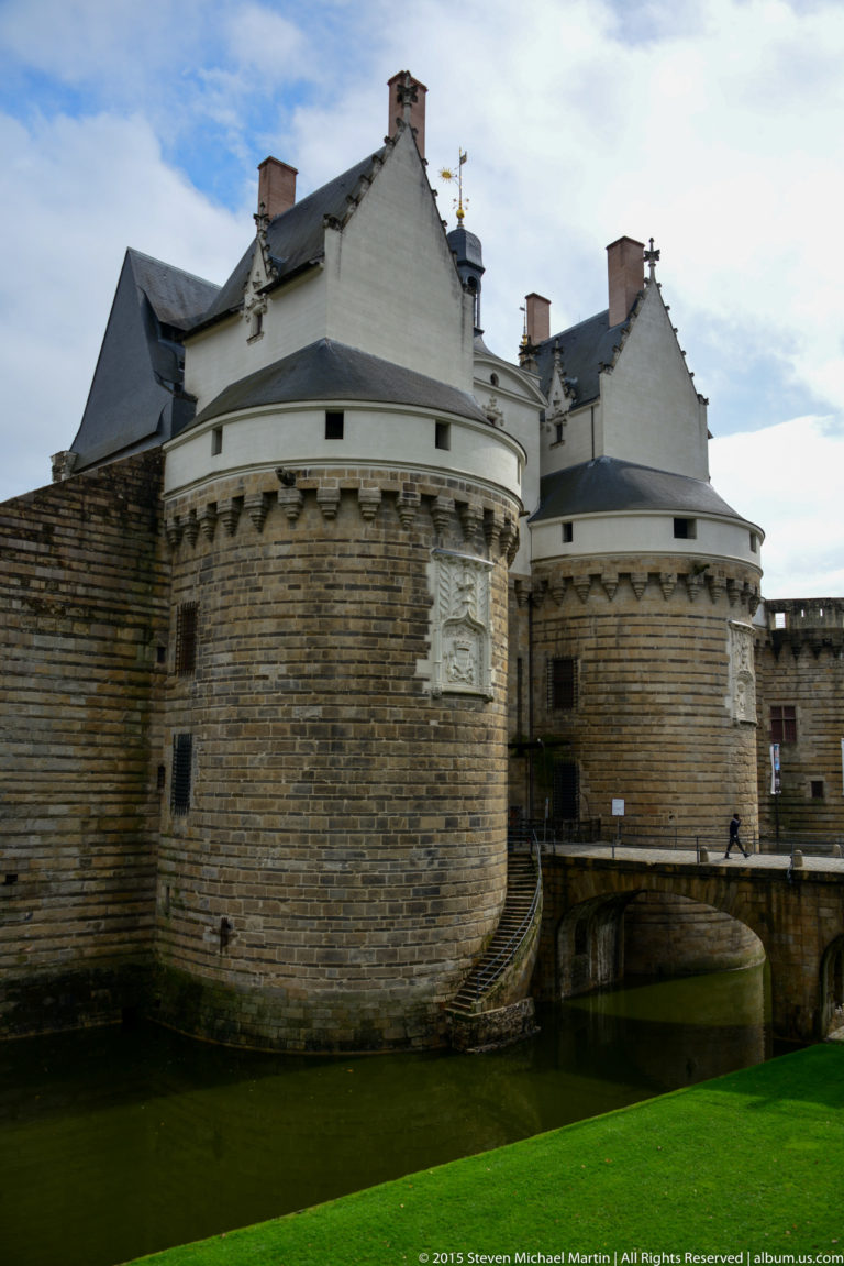 Two round stone towers of the Château des ducs de Bretagne rise from the moat beside a stone bridge.