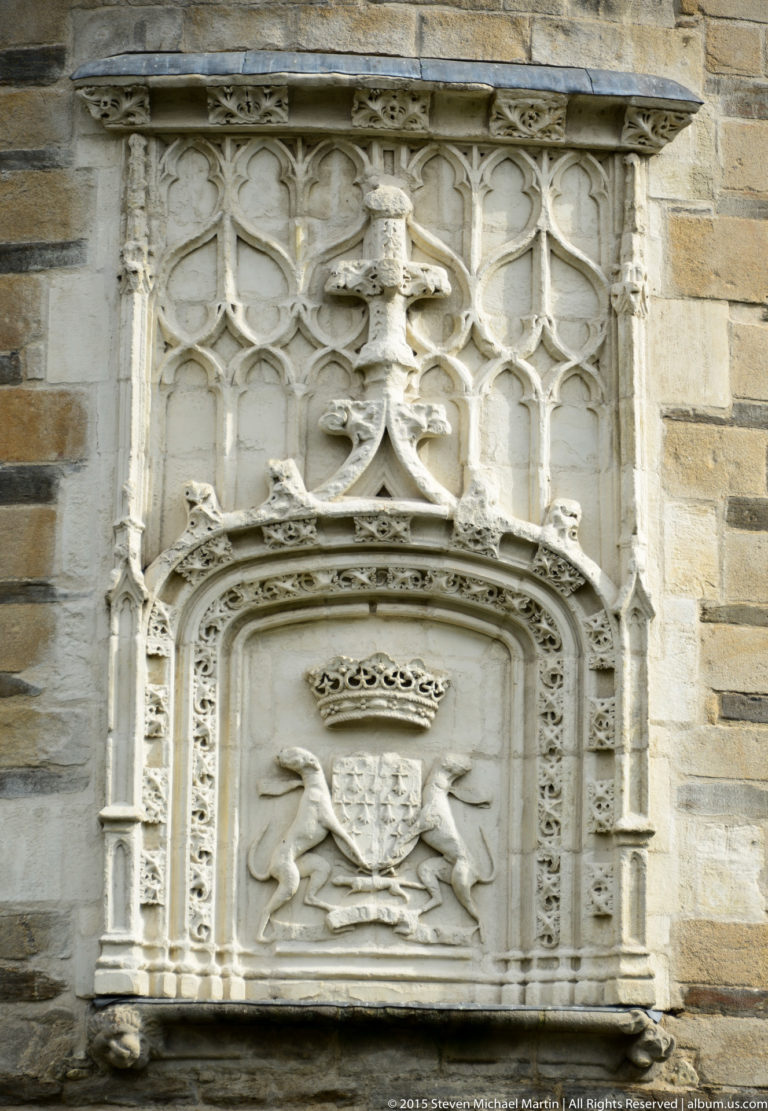 Carved stone heraldic panel with a crowned shield and supporting animals set into the château's darker masonry wall.