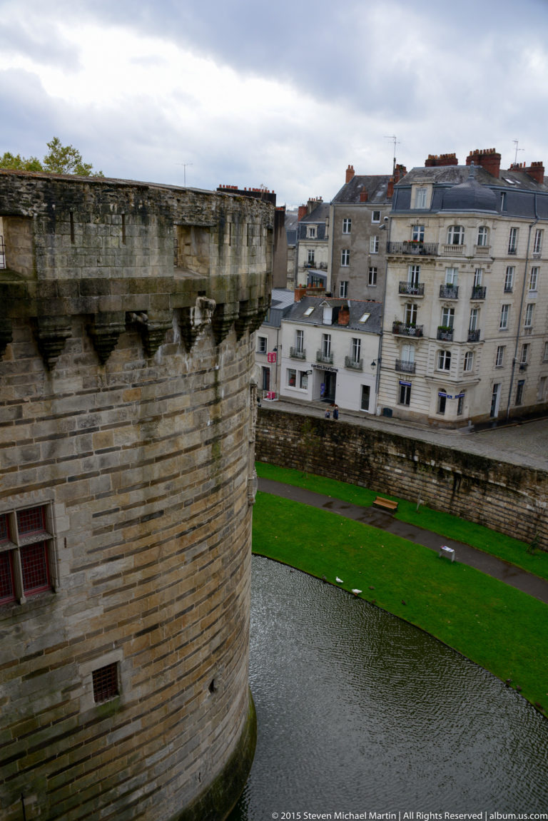 Large round château tower beside the moat, viewed from above with apartment buildings across the water.