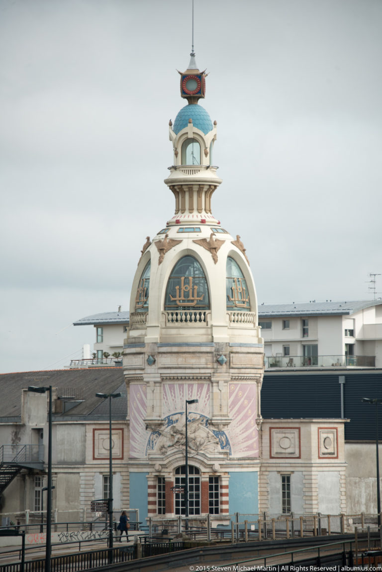 Ornate historic Nantes building with pale blue and pink decoration, small dome, classical moldings, and rooftop finial.