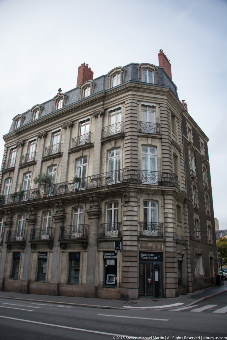 Large corner apartment building with wrought-iron balconies, tall windows, rusticated stone, and a dark mansard roof.