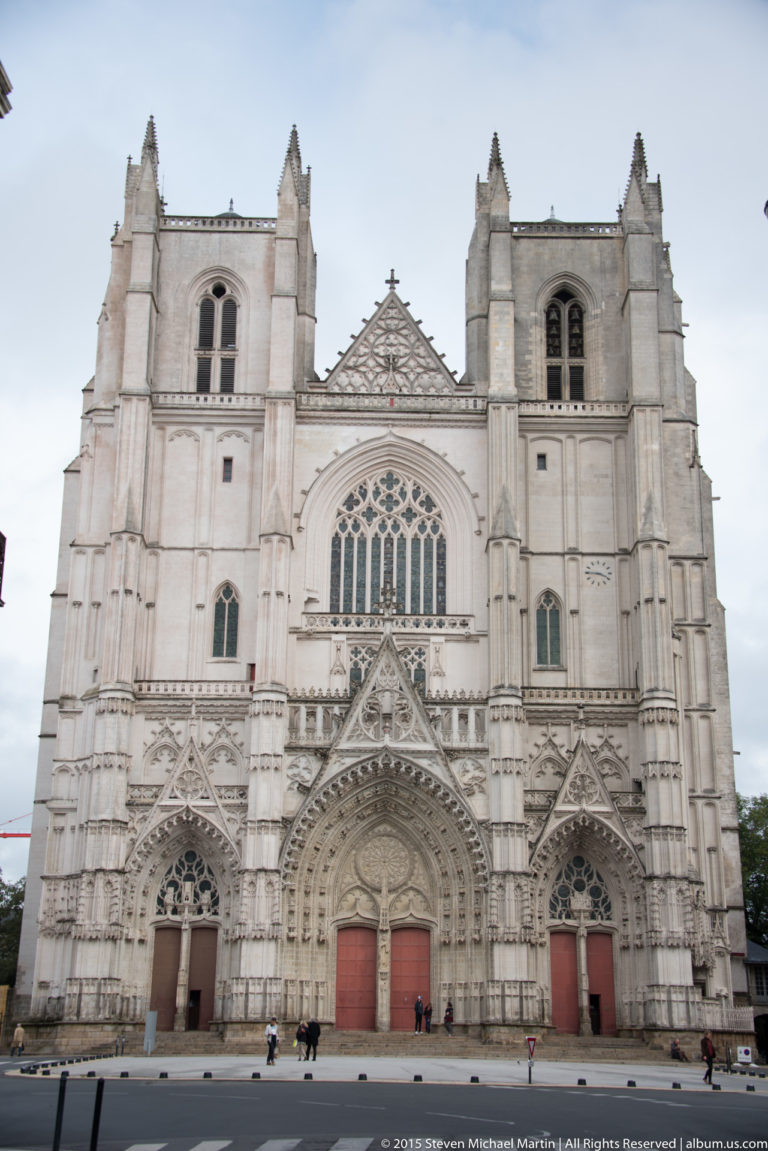 Frontal west façade of Nantes Cathedral with three Gothic portals, large central window, buttresses, and twin towers.