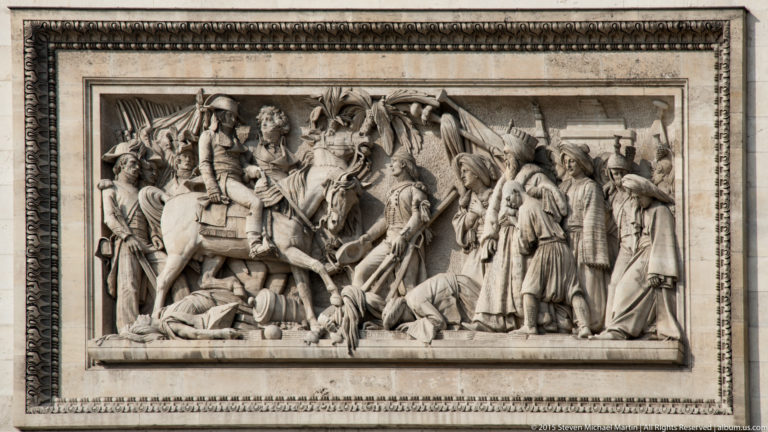 Rectangular stone bas-relief crowded with soldiers and military figures in a historical scene on the Arc de Triomphe.