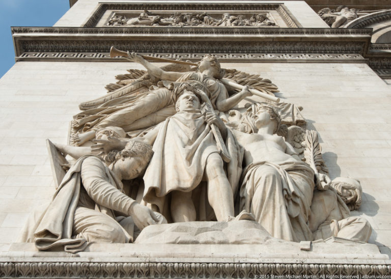 Frontal low-angle close view of an Antoine Étex high-relief group with clustered figures and deep drapery on the Arc de Triomphe.