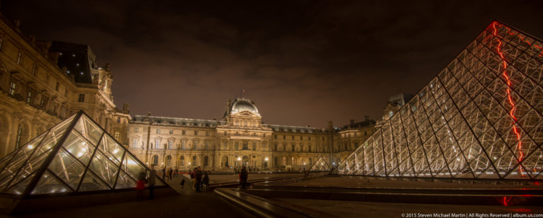Large Louvre Pyramid at right and smaller glass pyramid at left within the illuminated Louvre Palace courtyard at night.