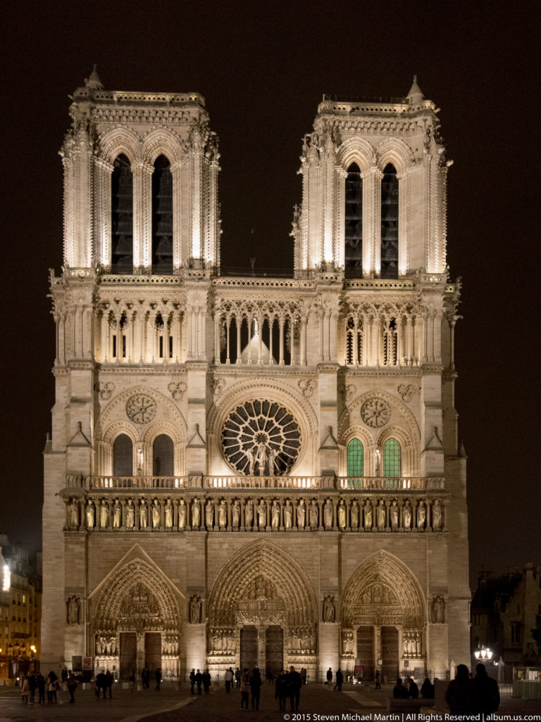 Illuminated Notre-Dame de Paris west façade at night, centered on the twin towers, rose window, galleries, and sculpted portals.
