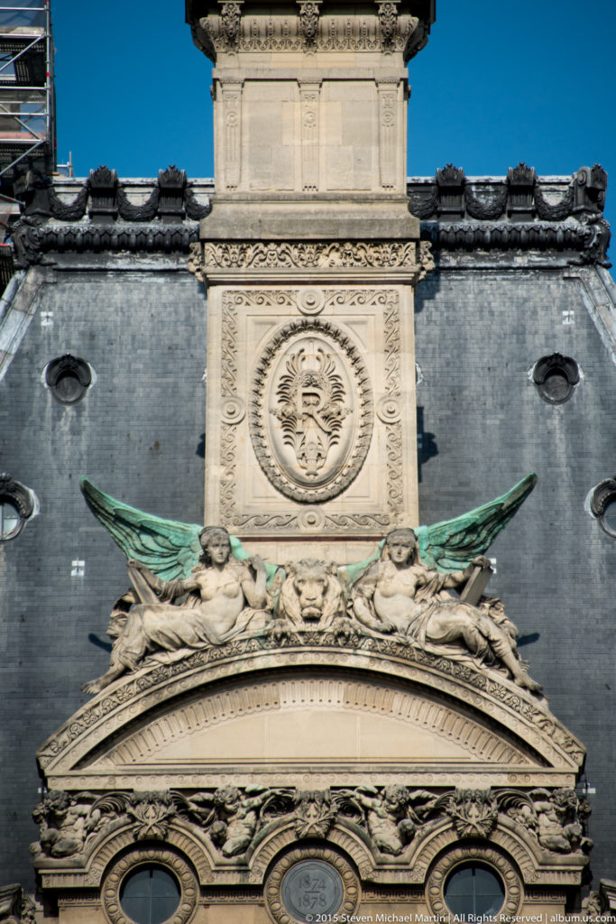 Close architectural detail of the Arc de Triomphe du Carrousel with winged sculpture, carved wreaths, medallion, and layered stone ornament.