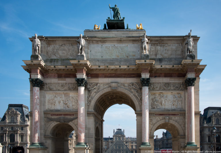 Arc de Triomphe du Carrousel with three arches, pink marble columns, rooftop statues, and the Paris axis visible through the center.