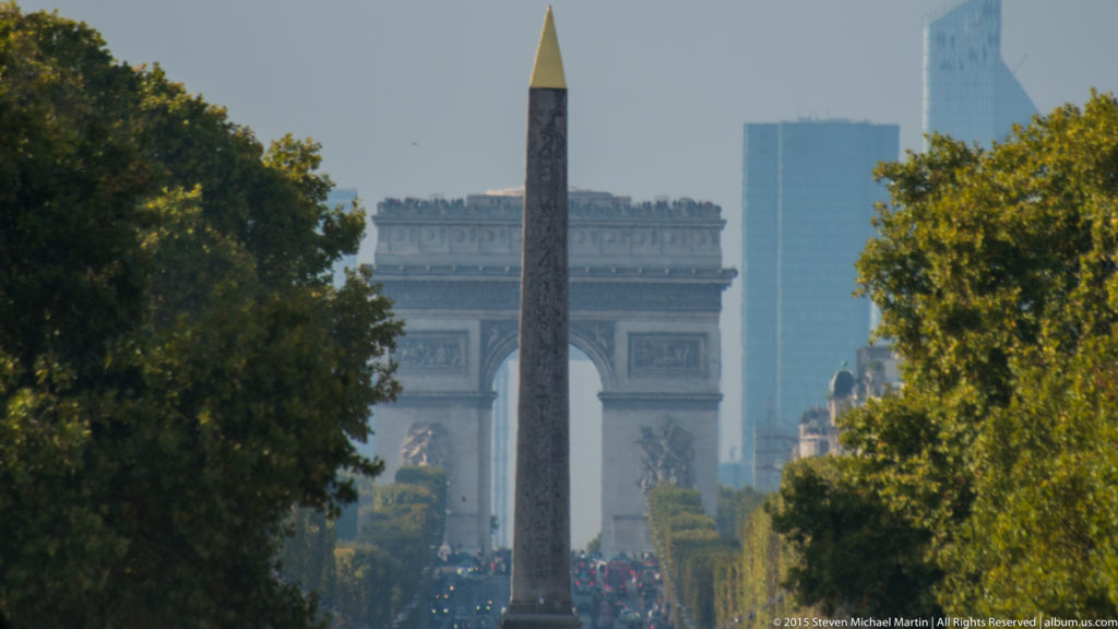 Luxor Obelisk framed by trees with the Arc de Triomphe centered in the distance along the Paris ceremonial axis.