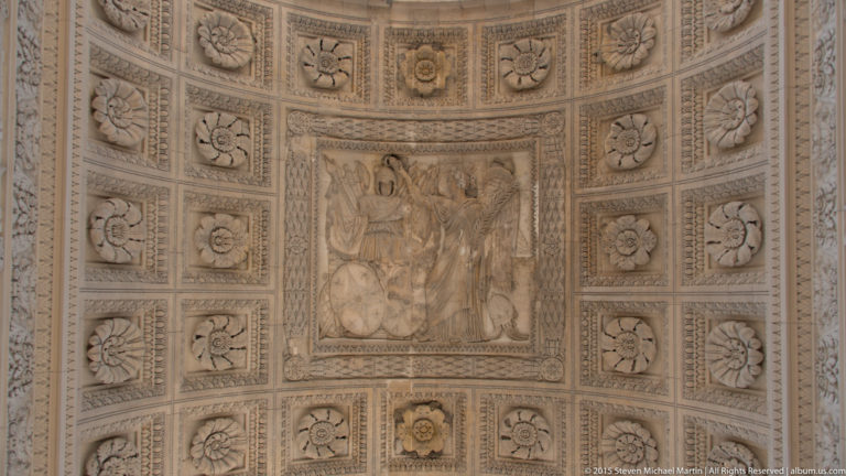 Upward view beneath the Arc de Triomphe du Carrousel showing a coffered vault filled with rosettes, reliefs, and carved ornament.