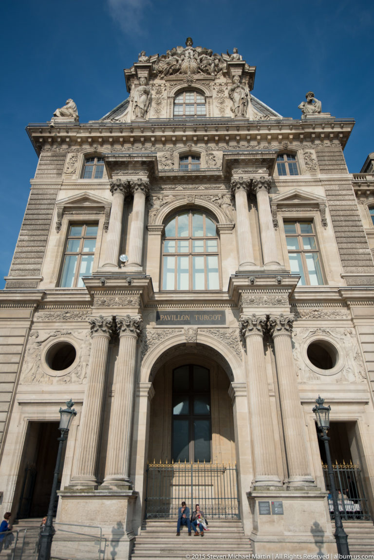 Upward view of the Louvre’s Pavillon Turgot with labeled central arch, paired columns, round openings, sculpture, and carved pediment.