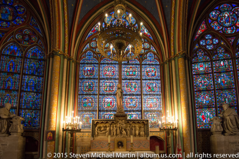 Side chapel with tall stained-glass windows, central sculpted altar, chandelier, columns, and painted vaulting.