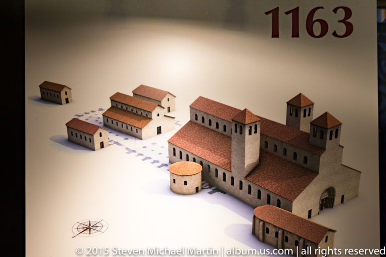 Scale model of a medieval church complex with red roofs and towers beneath the large date 1163.