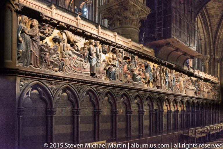 Oblique view along a long polychrome biblical relief beneath a continuous Gothic architectural canopy.