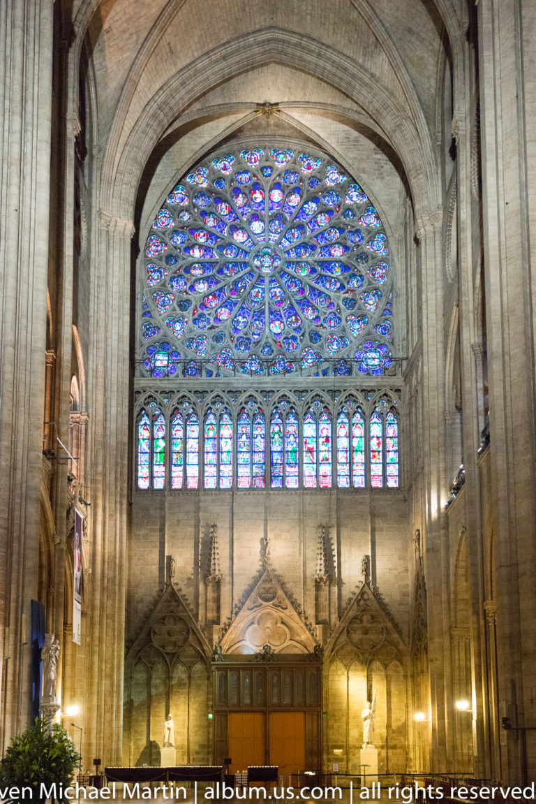 Large circular stained-glass rose window above a row of lancet windows and dark interior furnishings.