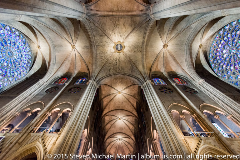 Centered upward view of paired rose windows, pointed arches, and ribbed vaults around the cathedral crossing.